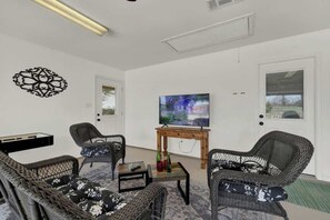 A furnished living room with wicker furniture, a flat-screen TV, and a door with a window. - Starlight Meadows Hot-tub 3mi to Downtown (Fredericksburg)
