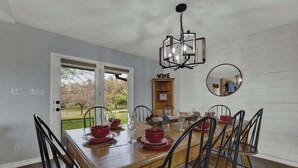 A dining room with a wooden table set for six, black chairs, a chandelier, a wine rack, and a mirror on the wall. - Starlight Meadows Hot-tub 3mi to Downtown (Fredericksburg)