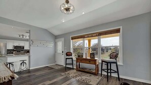 A modern kitchen with a built-in microwave and a dining area with a wooden table and two bar stools. - Starlight Meadows Hot-tub 3mi to Downtown (Fredericksburg)