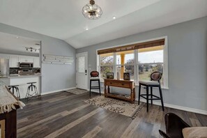 A modern kitchen with a built-in microwave and a dining area with a wooden table and two bar stools. - Starlight Meadows Hot-tub 3mi to Downtown (Fredericksburg)