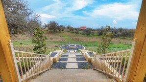 A wooden staircase leading to a circular seating area surrounded by a white railing, set against a rural landscape with trees and a distant building. - Starlight Meadows Hot-tub 3mi to Downtown (Fredericksburg)