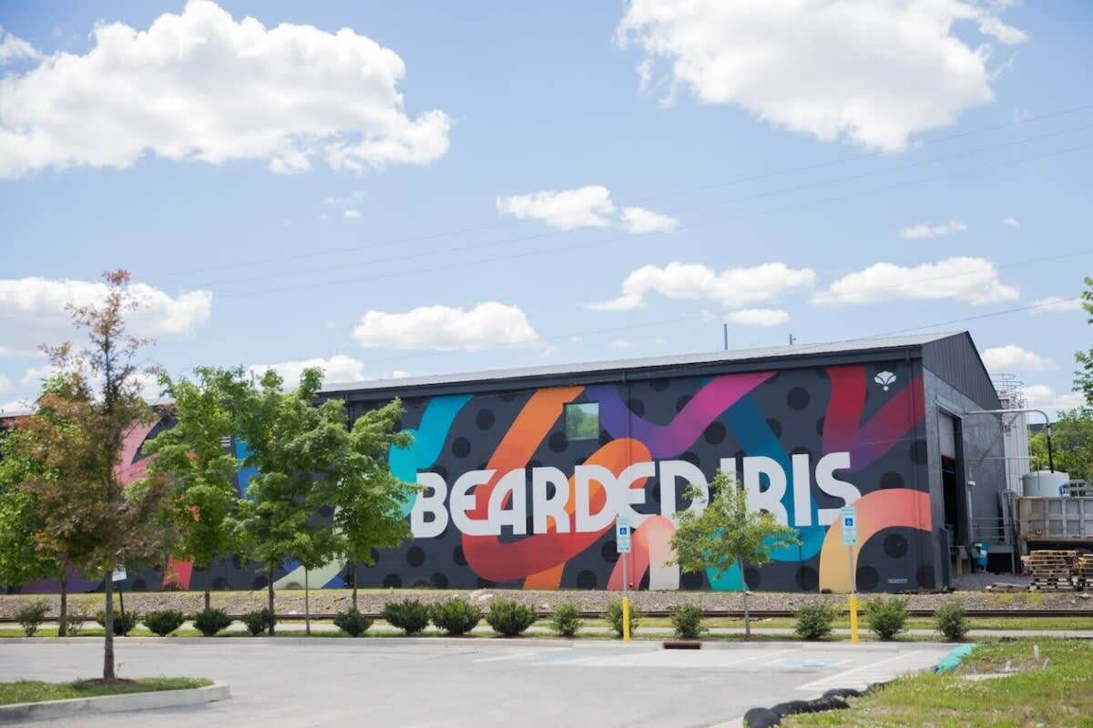 Un edificio con un mural colorido en la fachada, un estacionamiento y algunos árboles.