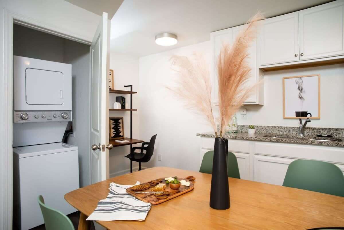 A compact kitchen with white cabinets, a built-in oven, and a dining area with a wooden table and chairs.
