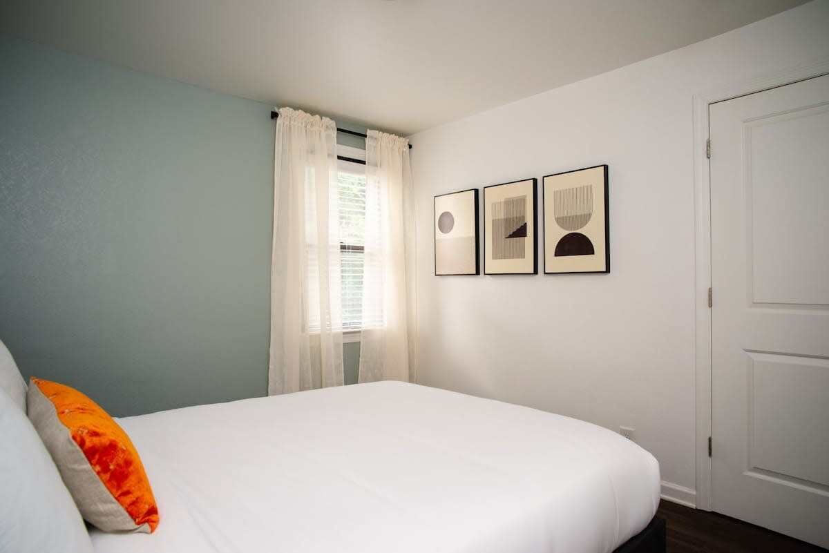 Ein Schlafzimmer mit einem Bett, einem Fenster mit Vorhängen und drei gerahmten Bildern an der Wand.