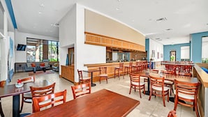 A modern dining area with wooden tables and chairs, a kitchen area with wooden cabinets, and a seating area with sofas and a TV.