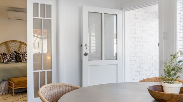 A room with a bed, a dining table, wicker chairs, and a white door with a window.