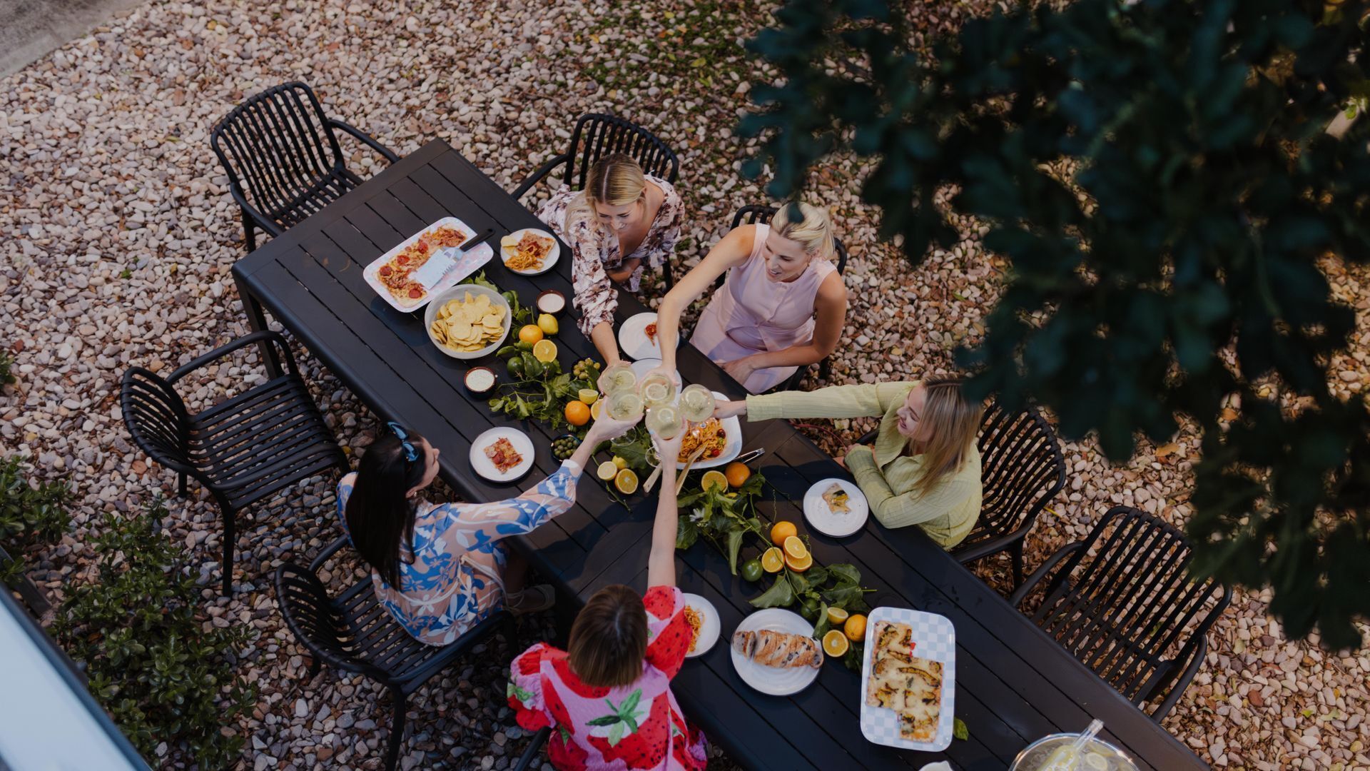 An outdoor dining area with a black table surrounded by chairs, various dishes, and drinks.