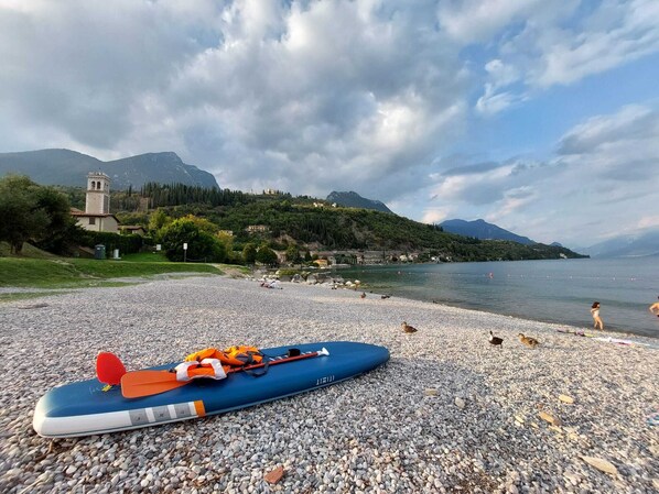 Ein Kiesstrand mit einer blauen Floße und orangefarbenen Rettungswesten am Ufer.