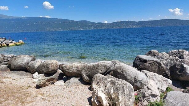 Una costa rocosa con aguas azul turquesa y montañas a lo lejos.