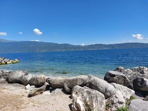 Eine felsige Küstenlinie mit klarem, blauem Wasser und Bergen im Hintergrund.