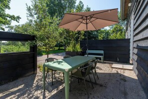 Eine Terrasse im Freien mit Tisch, Stühlen, einem großen Sonnenschirm und einem Holzzaun.