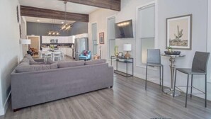 A modern living room with a grey sofa, a dining area with two chairs, a kitchen in the background, and a ceiling fan. - Gorgeous, Family-Friendly Home Near Downtown (San Antonio)