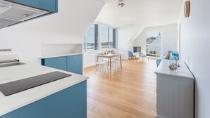 A modern kitchen with a large island, a dining area with a table and chairs, and a view of the outdoors. - La Grande Plage - Three Bedroom Apartment, Sleeps 5 (Saint-Cast-le-Guildo)