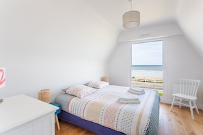 Un dormitorio con cama, escritorio, silla y vista al mar.