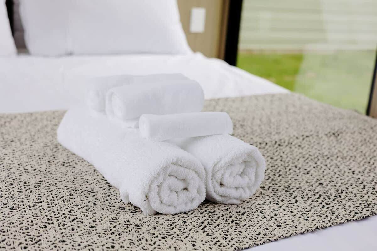 Un lit bien fait, avec du linge de lit blanc et une serviette enroulée posée sur un tapis texturé.