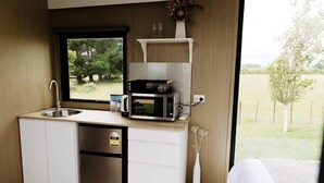 A compact kitchenette with a sink, microwave, and small refrigerator. A window offers a view of greenery outside. - Rural Delight by Tiny Away (Ohaupo)
