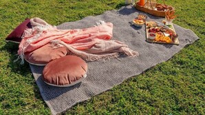 A picnic setup on a blanket with pillows, a basket of food, and a lantern.