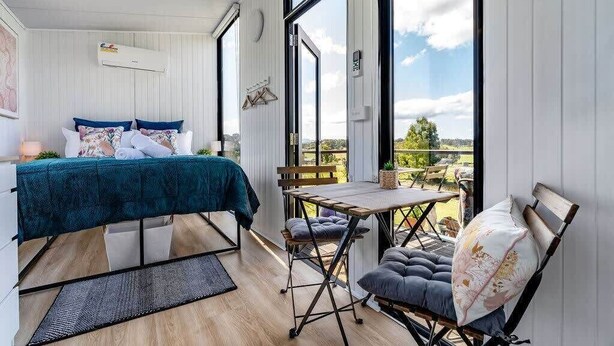 A bedroom with a bed, a small table, and a chair. There is a window with a view of the outdoors.