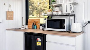 A compact kitchen with a microwave, coffee maker, and a small refrigerator. A window provides a view of greenery outside.