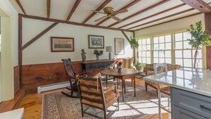 A dining area with wooden beams, a ceiling fan, a table with chairs, and a window with a view. - A Quintessential New England Historical Guesthouse (Groton)