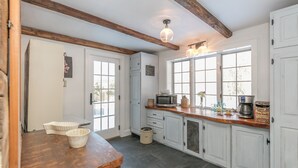 A kitchen with white cabinets, a wooden countertop, a microwave, a coffee maker, and a window with a view. - A Quintessential New England Historical Guesthouse (Groton)