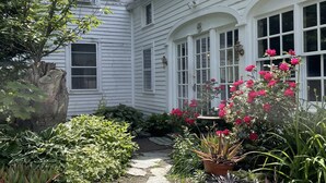 A white house with a stone pathway leading to the front door, surrounded by various potted plants and flowers. - A Quintessential New England Historical Guesthouse (Groton)
