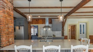 A spacious dining area with a large island, white chairs, and hanging pendant lights. - A Quintessential New England Historical Guesthouse (Groton)