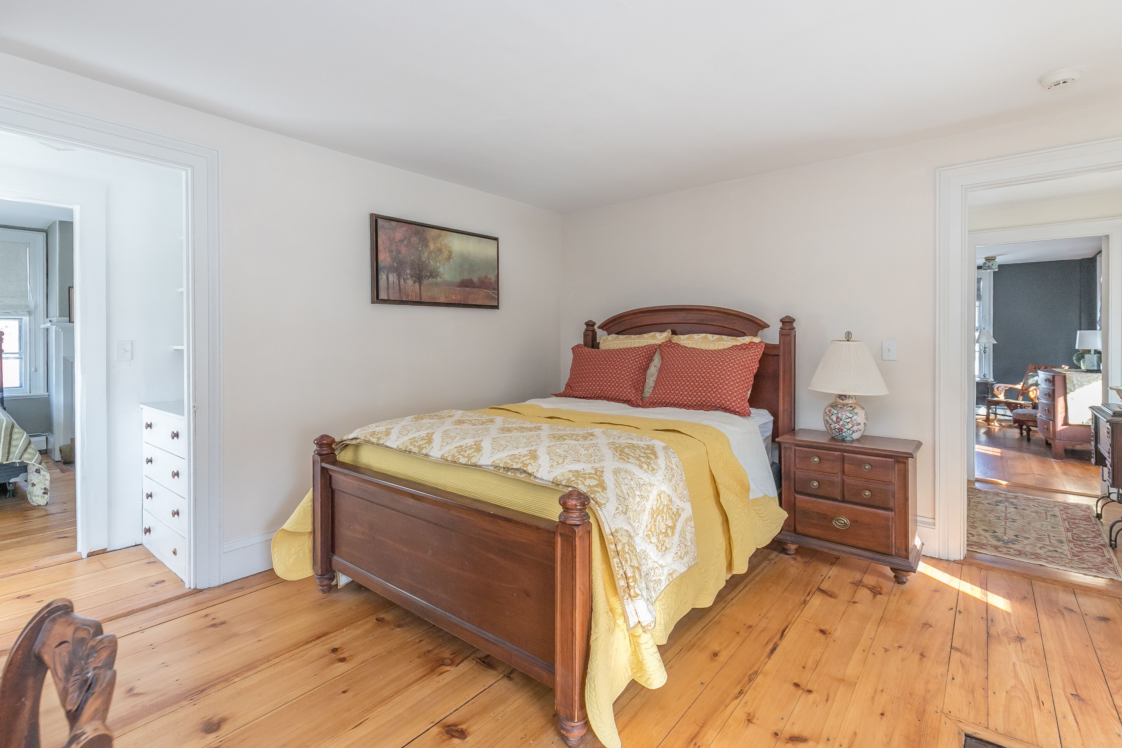 Une chambre à coucher avec un lit en bois, une table de chevet, une lampe et un tableau accroché au mur.