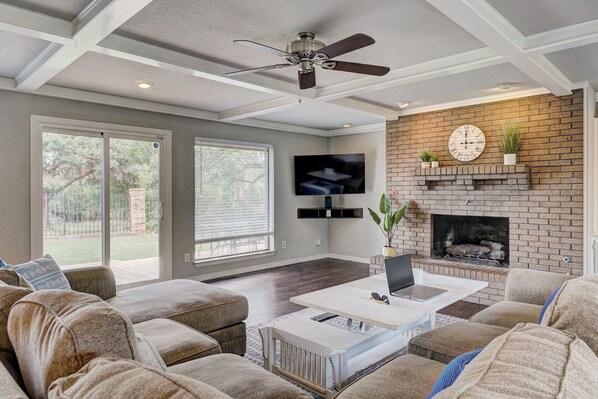 A spacious living room with a fireplace, a ceiling fan, and a large TV mounted on the wall.