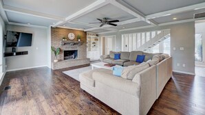 Amplia sala de estar con piso de madera, un sofá seccional color beige, una chimenea y una escalera que sube a otro nivel.