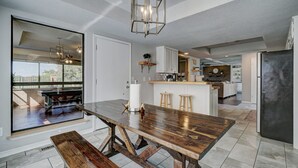 Una cocina moderna con una mesa de comedor de madera, taburetes de bar y un ventanal con vistas a un patio.