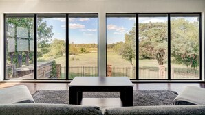 Un salón moderno con un amplio ventanal que da a un jardín césped y árboles.