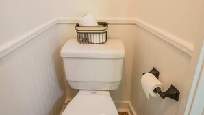 Des toilettes blanches avec un abattant blanc, un porte-rouleau de papier toilette blanc et, au mur, un tableau représentant une fleur blanche.