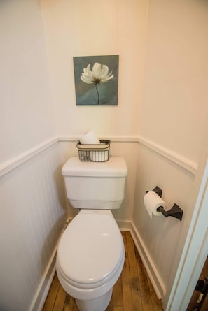 Des toilettes blanches avec un abattant blanc, un porte-rouleau de papier toilette blanc et, au mur, un tableau représentant une fleur blanche.