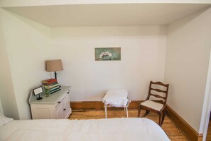 Une chambre à coucher avec un lit, une table de chevet sur laquelle se trouvent des livres et une lampe, une chaise et un tableau accroché au mur.
