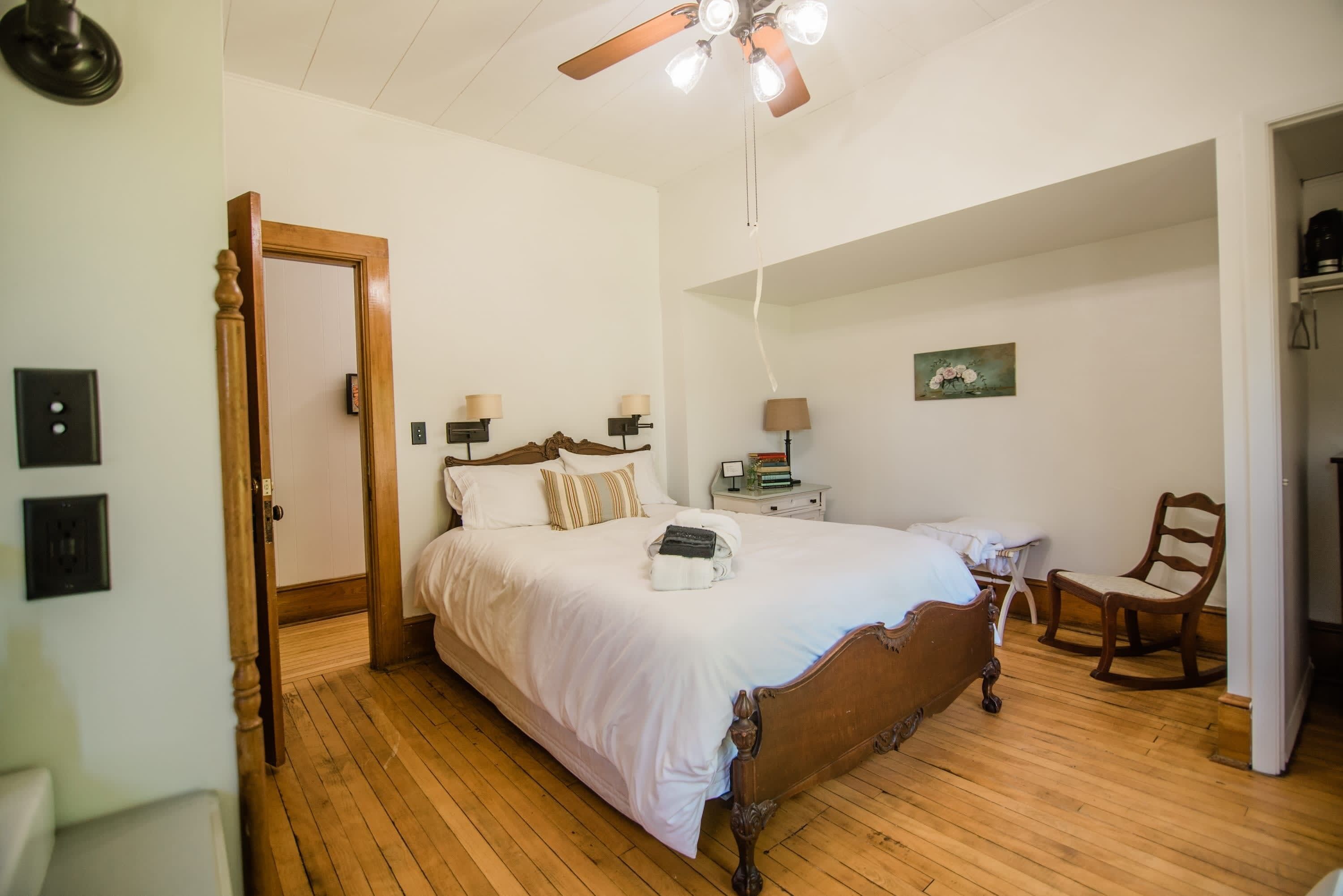 Un dormitorio con una cama de madera, una mesita de noche, una silla, un ventilador de techo y un cuadro en la pared.