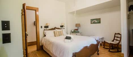 A bedroom with a wooden bed, a nightstand, a chair, a ceiling fan, and a painting on the wall.