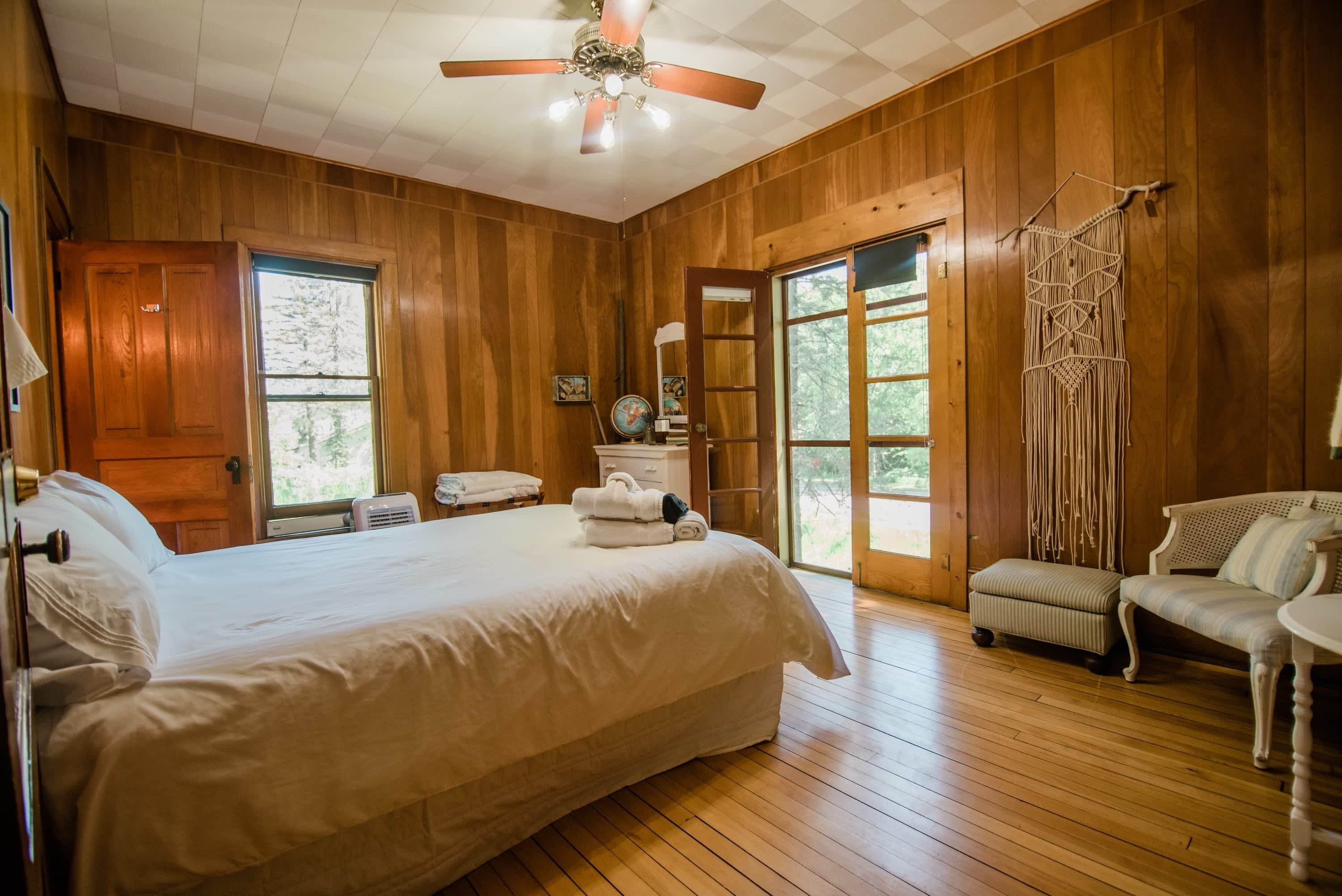 A wooden-paneled bedroom with a large bed, a ceiling fan, and a view of the outdoors.