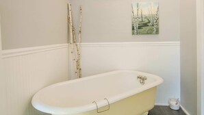 Ein Badezimmer mit freistehender Badewanne, einem Bild an der Wand und Holzboden.