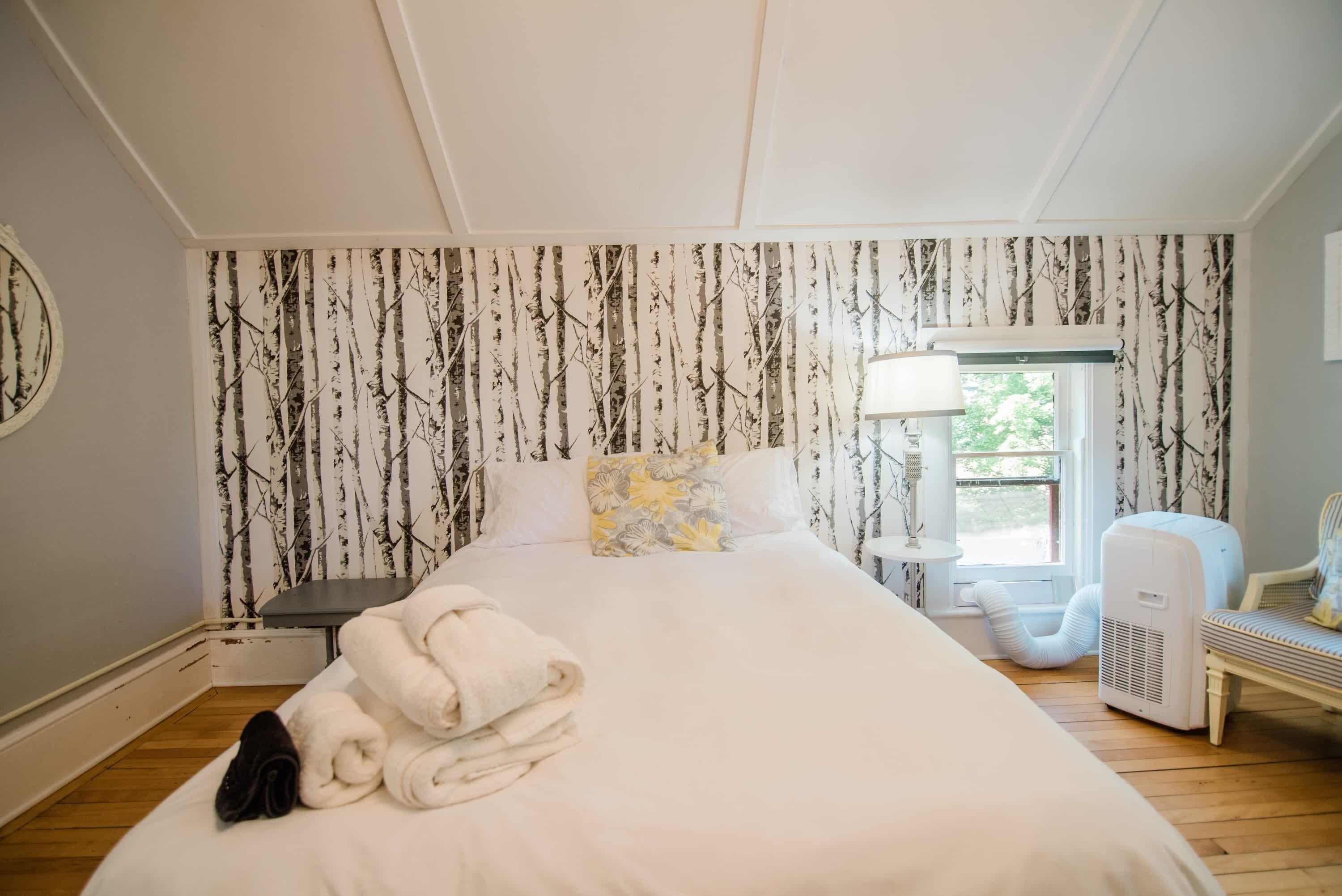 Une chambre d’hôtel avec un lit, une table de chevet, une lampe, un radiateur et une fenêtre donnant sur des arbres.