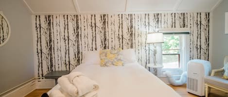 Une chambre d’hôtel avec un lit, une table de chevet, une lampe, un radiateur et une fenêtre donnant sur des arbres.