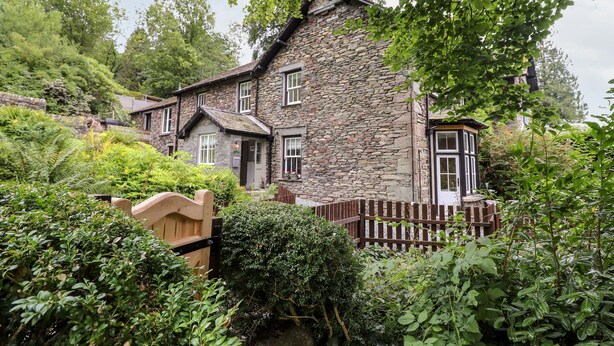 A stone house with a wooden gate, surrounded by lush greenery and a stone wall. - Eller Close House (Ambleside)