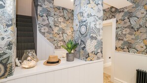 A hallway with patterned wallpaper, a staircase, and a white counter with decorative items. - Eller Close House (Ambleside)