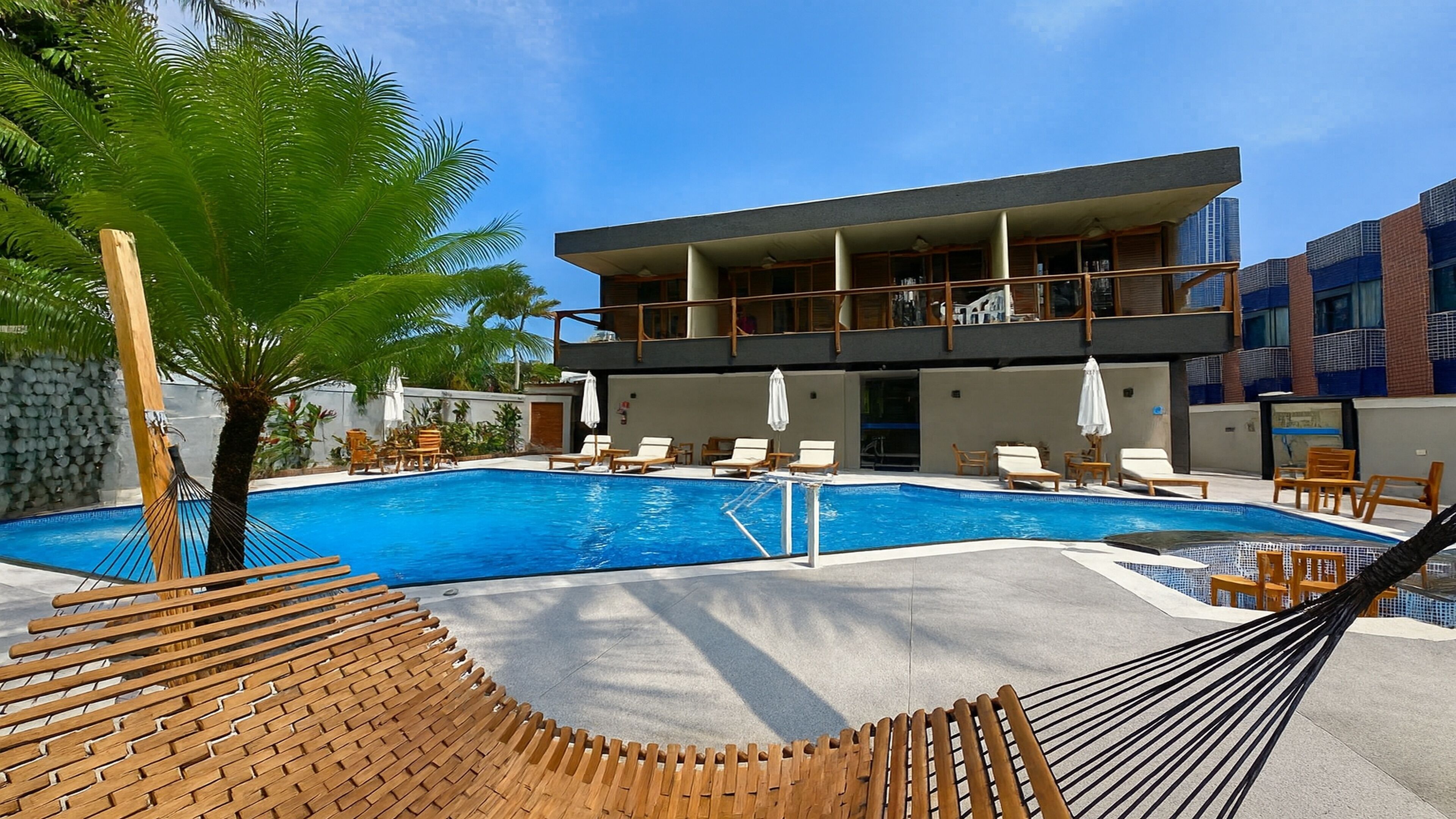 A modern hotel with a pool area, including lounge chairs and a hammock.