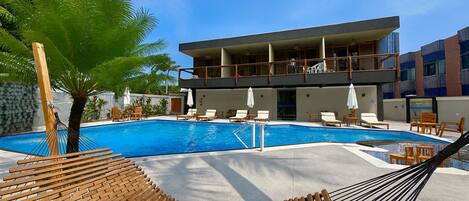 A modern hotel with a pool area, including lounge chairs and a hammock.