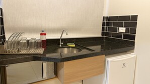A kitchen with a black countertop, stainless steel sink, and a white refrigerator. - Marmeu Tropical Ltda (Guarujá)