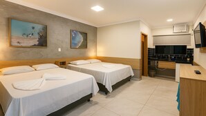 A hotel room with two beds, a kitchenette, and artwork on the walls. - Marmeu Tropical Ltda (Guarujá)