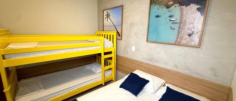 A room with bunk beds and a single bed, a painting of a beach scene, and a plain wall.