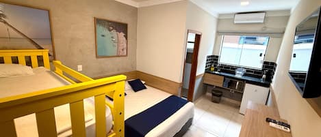 A hotel room with two beds, a kitchenette, a bathroom, and a large window.