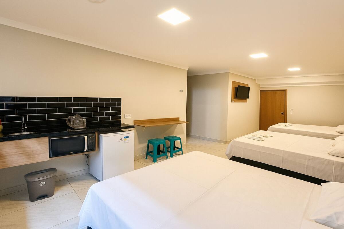 A hotel room with two beds, a small kitchenette, a TV, and a wooden headboard.